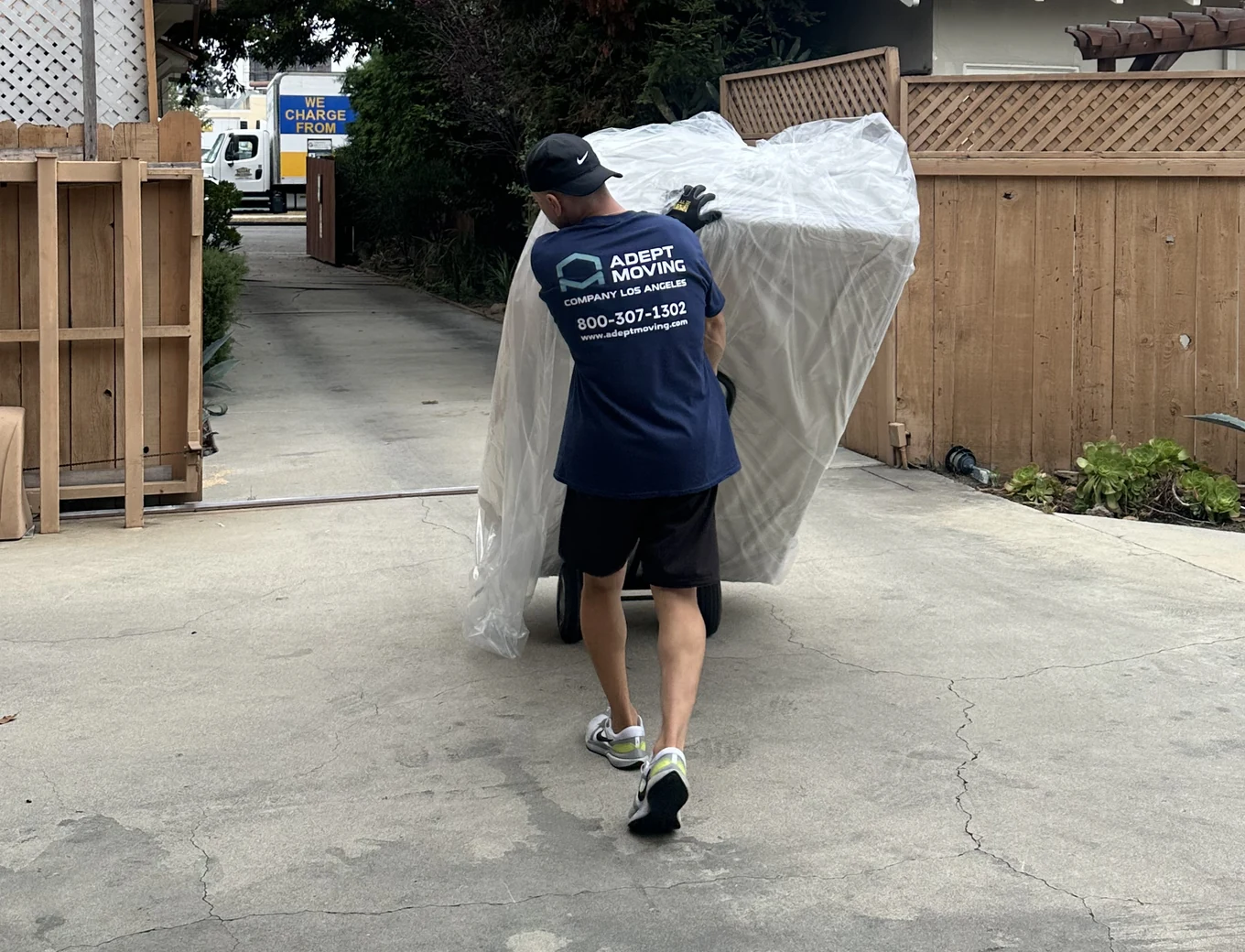 Adept mover carrying a wrapped mattress up a driveway on South Carmelina Avenue in Los Angeles, 90025
