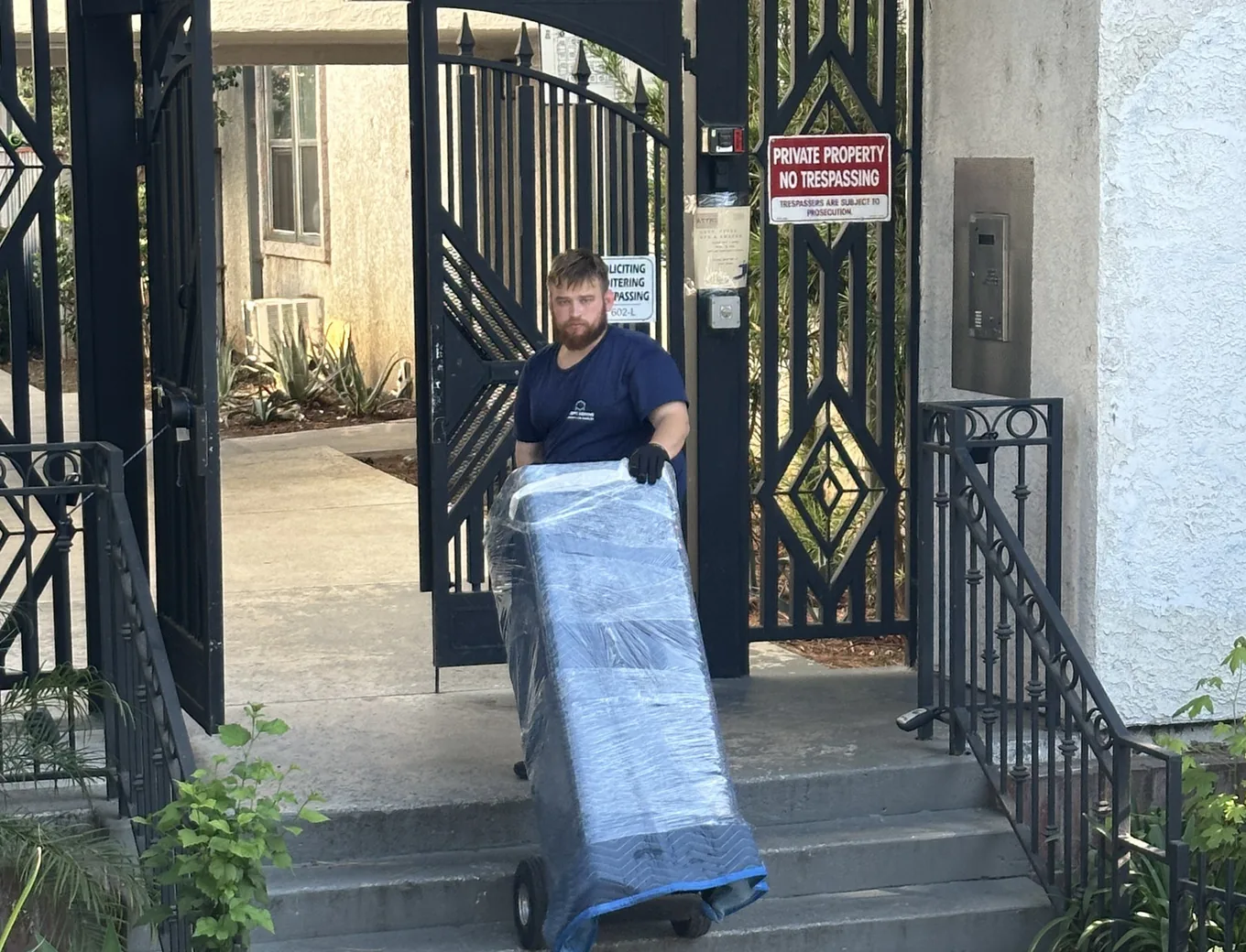 Adept Moving mover wheeling a wrapped piece down the steps from the gate of a condo complex on Hatteras Street in Tarzana