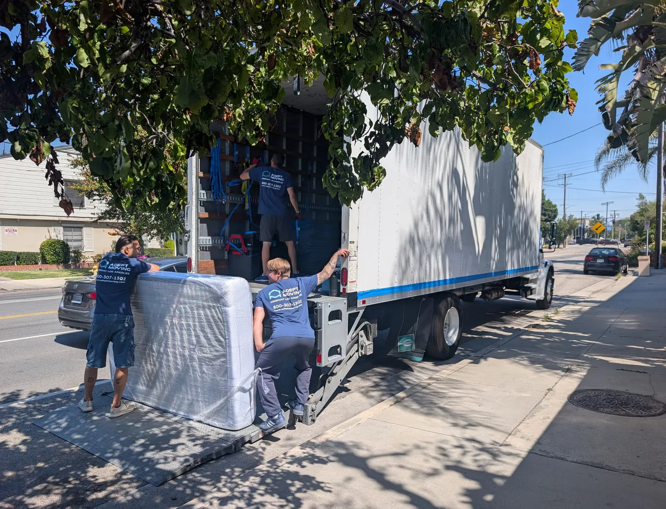 Adept Moving movers loading a shrink-wrapped mattress onto the truck liftgate on Whitsett Avenue in Valley Village, 91607