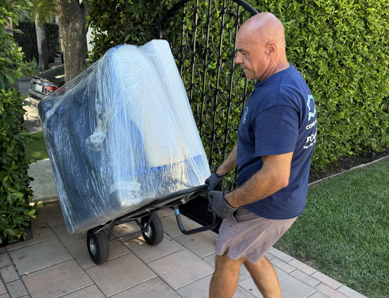 Adept mover easing a wrapped sofabed through the wrought-iron gate of a West Hollywood courtyard building