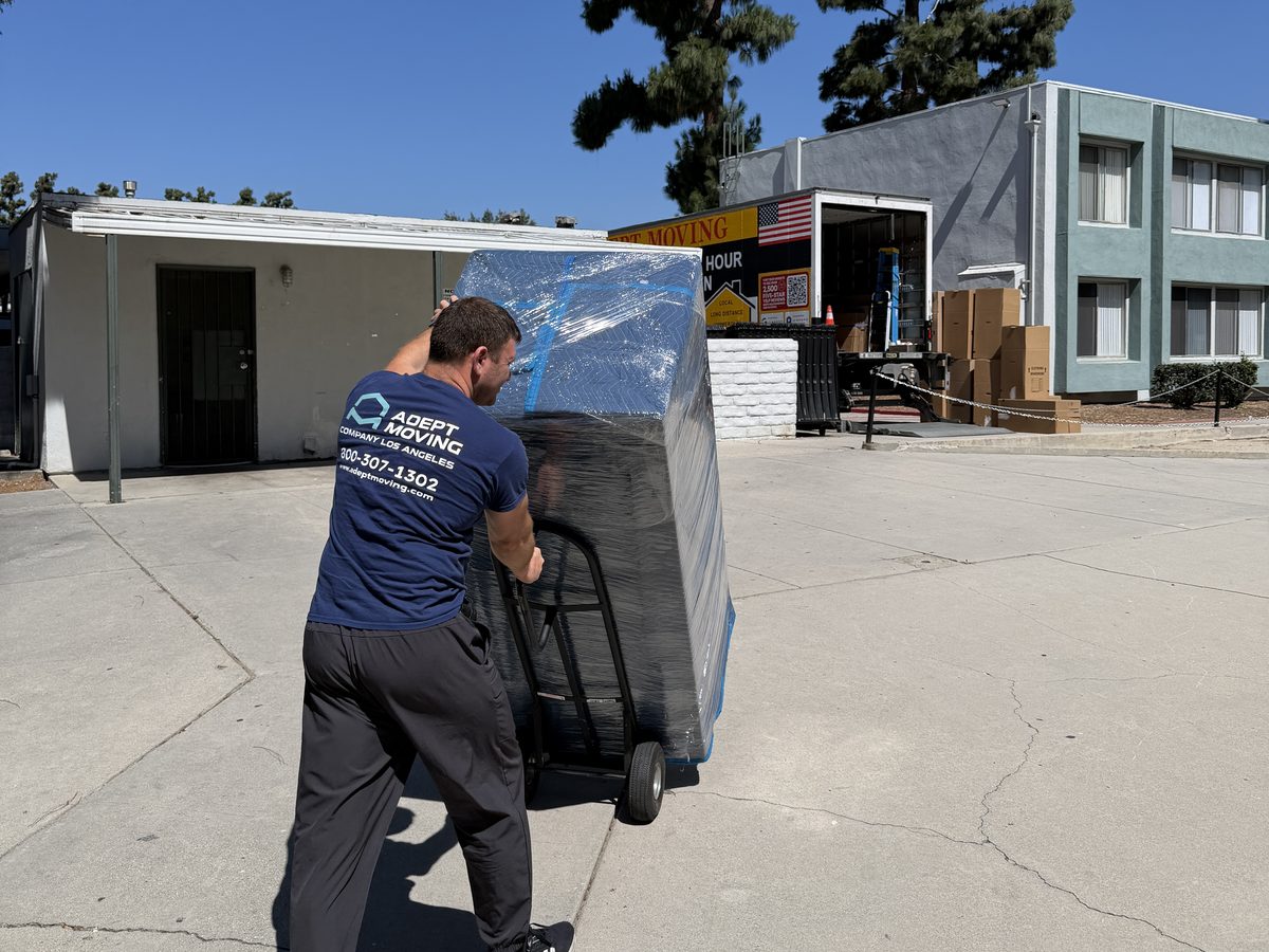 Adept Moving mover wheeling wrapped furniture on a dolly to the truck on Vintage Street