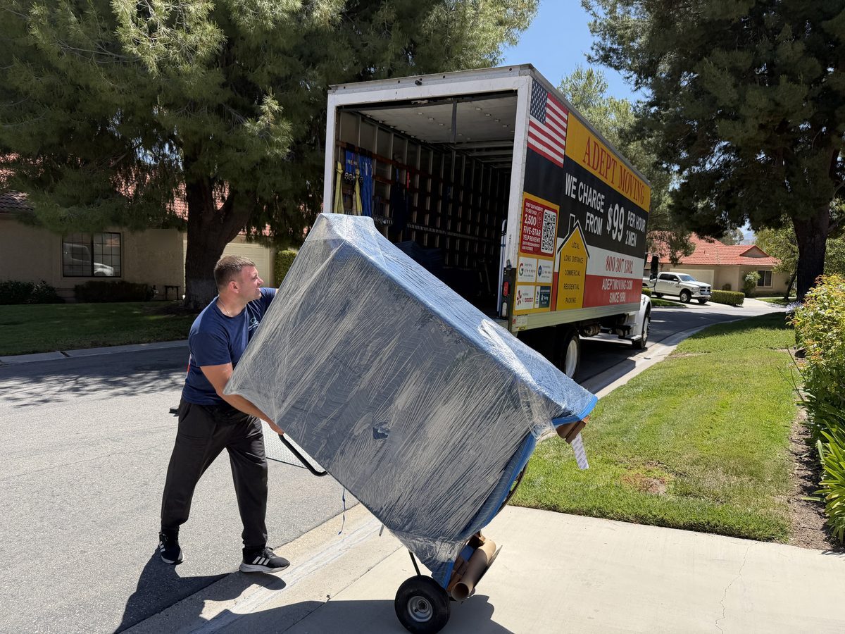Adept Moving mover wheeling a shrink-wrapped vintage dresser on a dolly to the truck