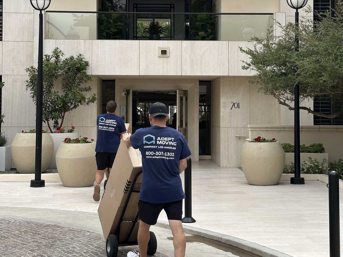 Adept Moving movers wheeling cartons across the motor court to the apartment building