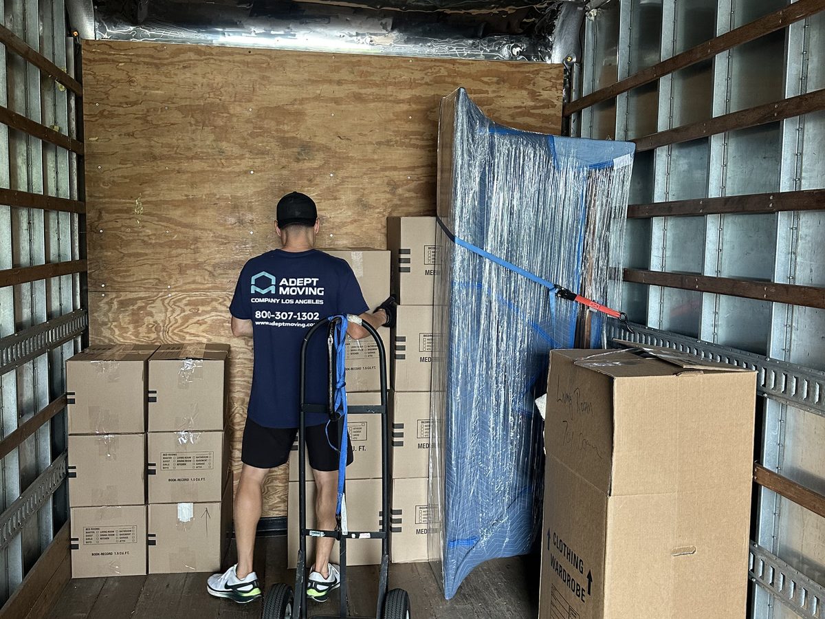 Adept Moving mover strapping wardrobe cartons and a wrapped mirror inside the truck