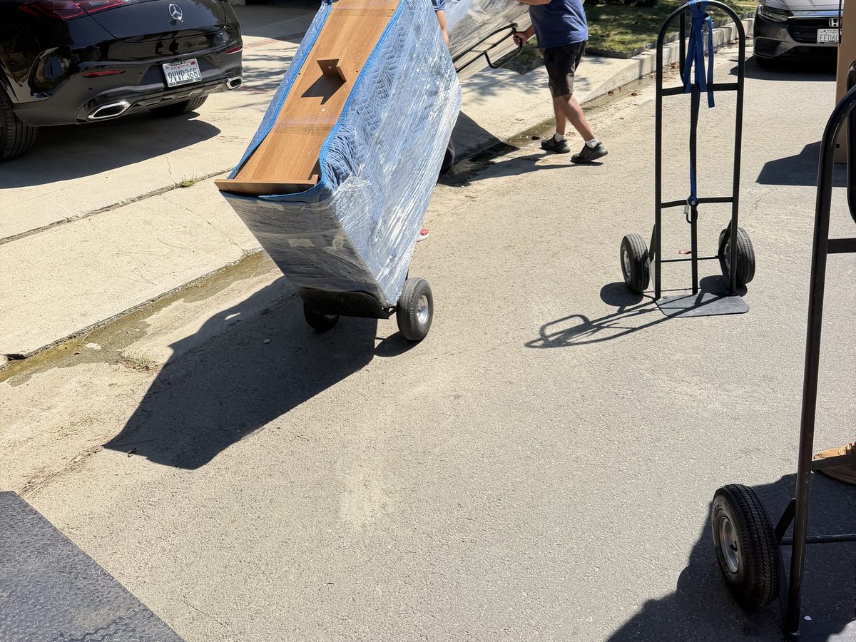 Adept Moving movers wheeling a shrink-wrapped headboard on a hand truck in Studio City