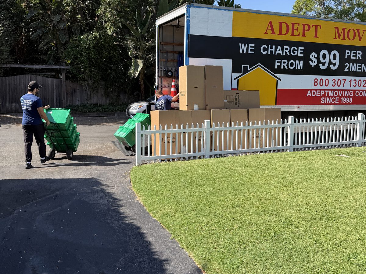 Adept Moving mover wheeling a stack of green plastic crates down the driveway to the truck