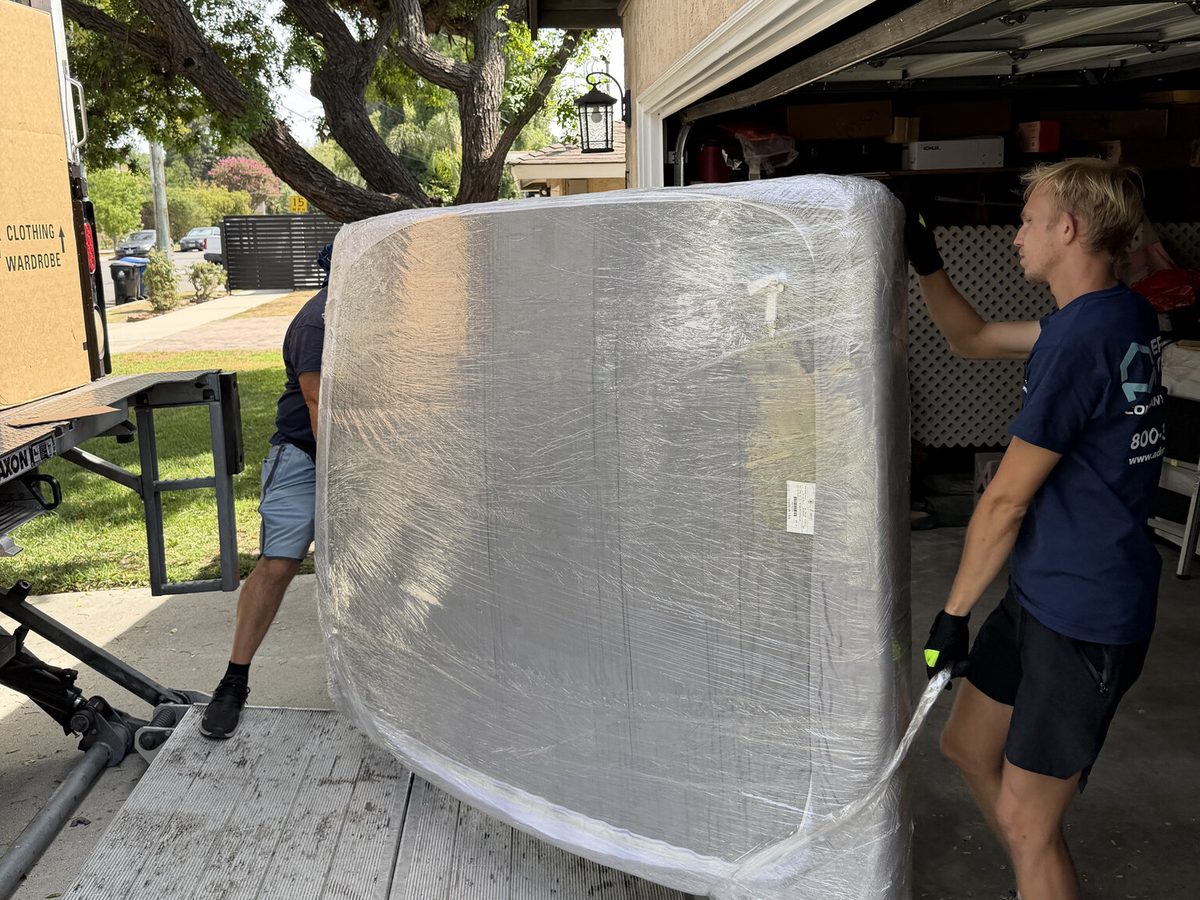 Adept Moving movers shrink-wrapping a box spring at the garage door in Valley Village