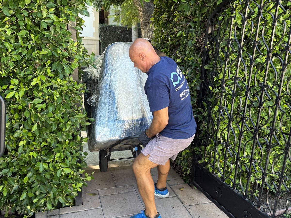 Adept Moving mover easing a wrapped sofabed through the wrought-iron gate of the West Hollywood apartment building