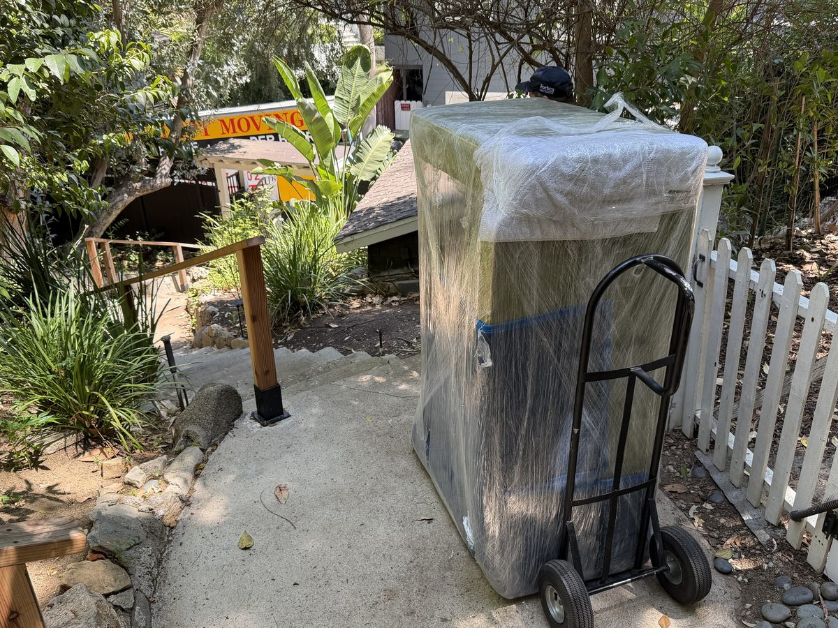 Wrapped gas grill on a hand truck beside the white picket fence at the Stanley Hills Drive drop-off