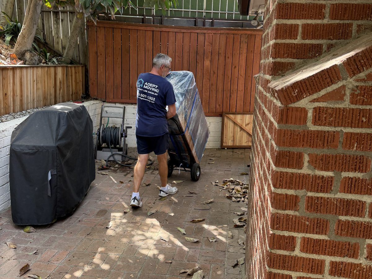 Adept Moving mover wheeling a blanket-wrapped piece past the covered gas grill in the Queens Road BBQ area