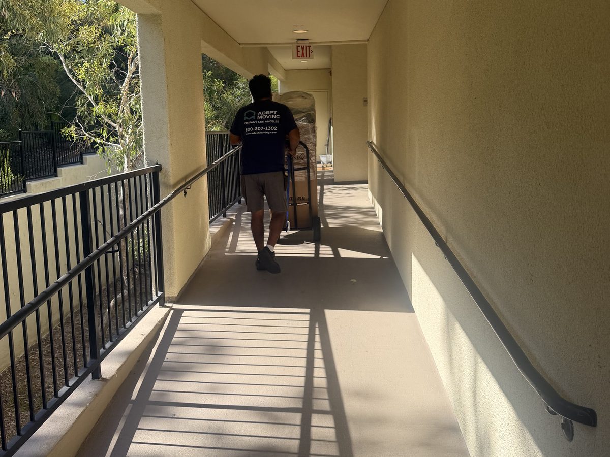 Adept Moving mover wheeling a dolly along the townhome walkway to the truck