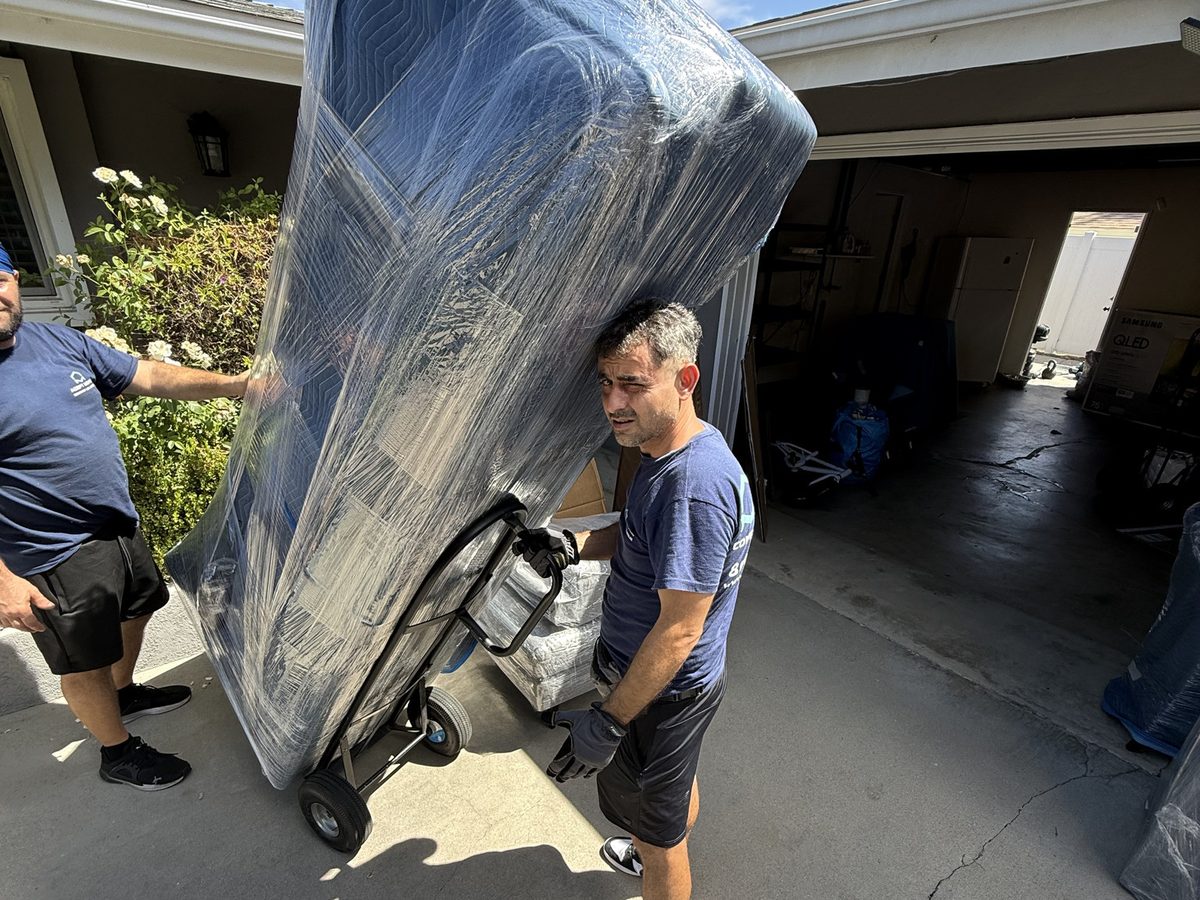 Adept Moving movers wheeling a wrapped piece of furniture on a dolly out through the garage