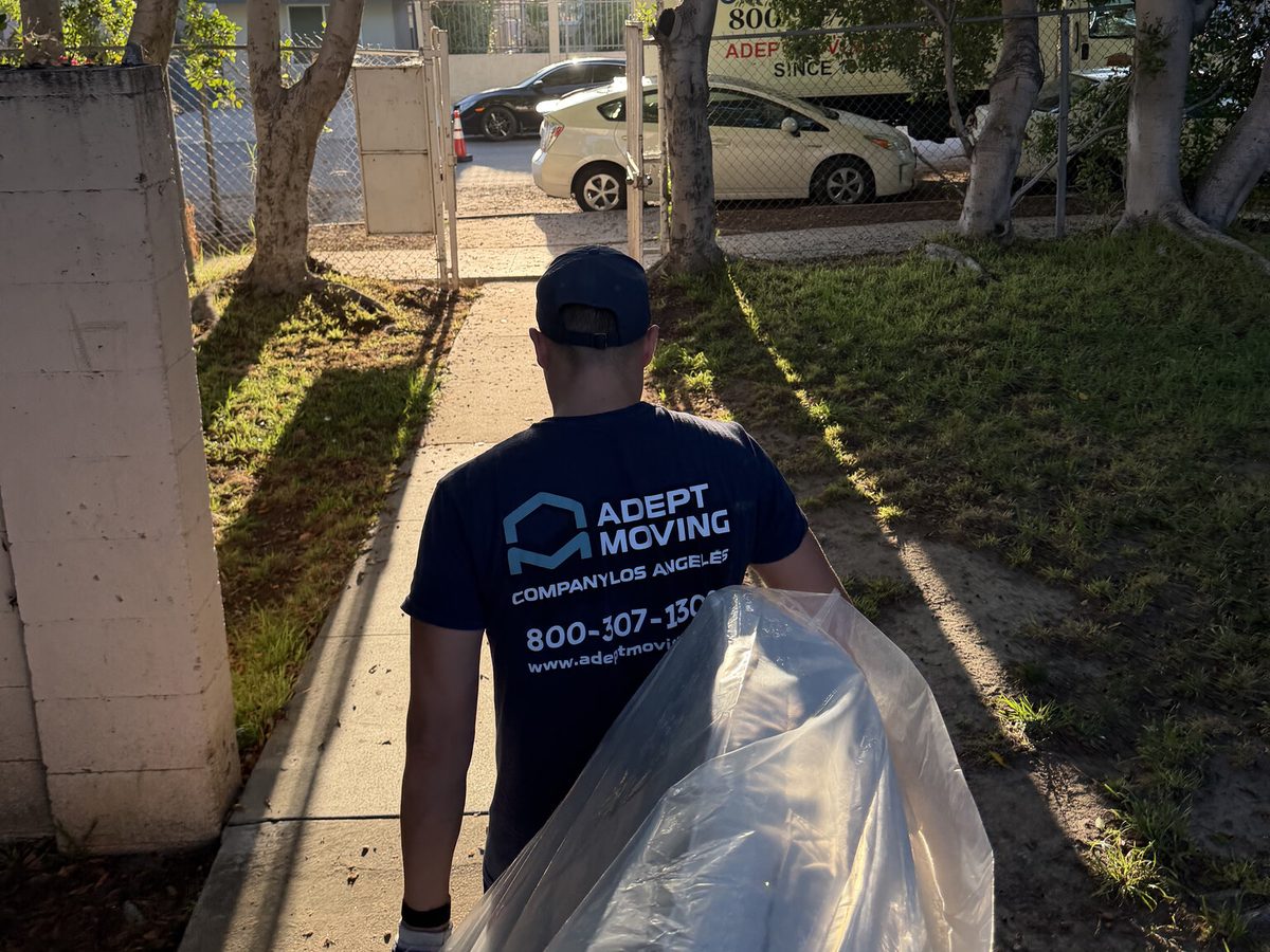 Adept Moving mover carrying a plastic-wrapped mattress along the sidewalk to the truck