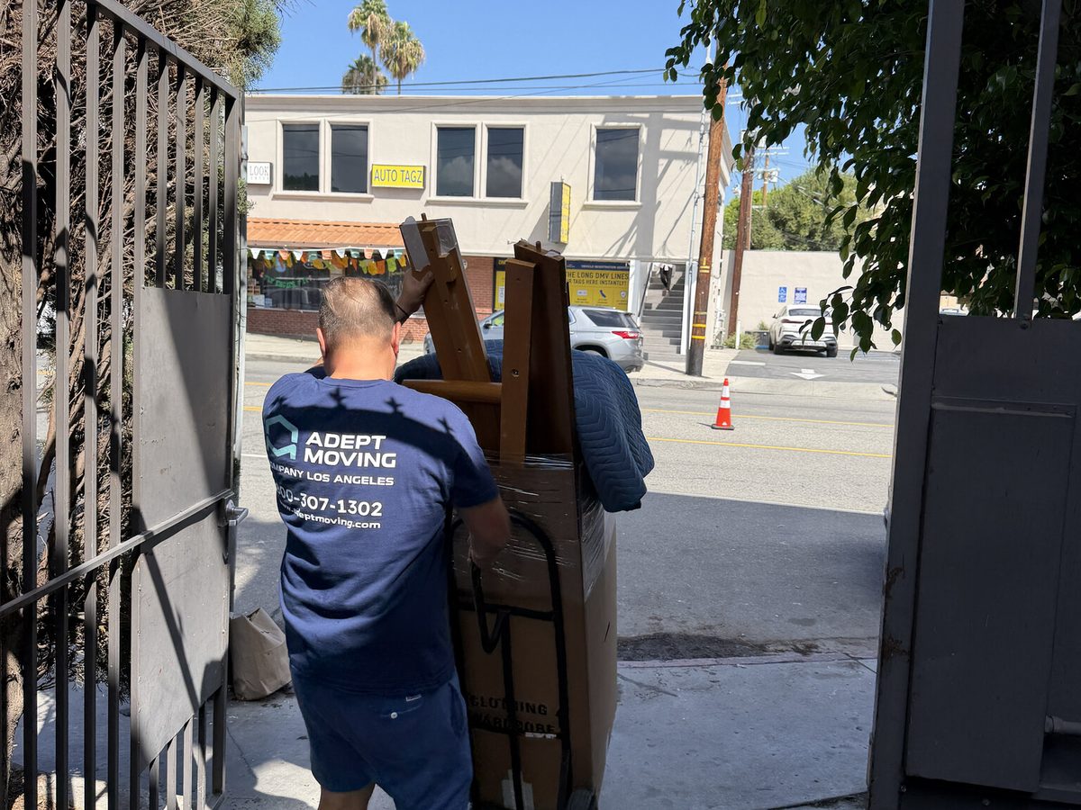 Adept Moving mover wheeling furniture on a hand truck through the building gate to Moorpark Street