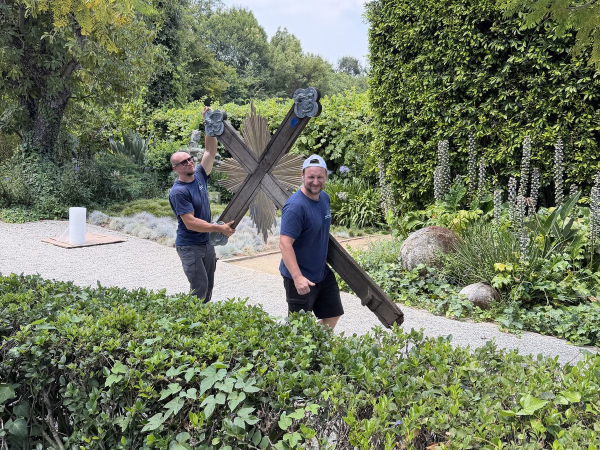 Adept Moving movers carrying the wooden cross past the garden hedges in South Pasadena