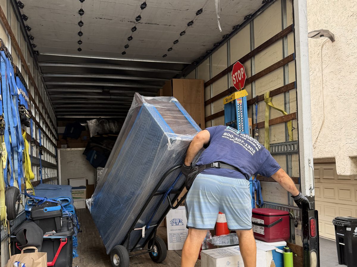 Adept Moving mover wheeling a blanket-wrapped piece on a hand truck inside the truck