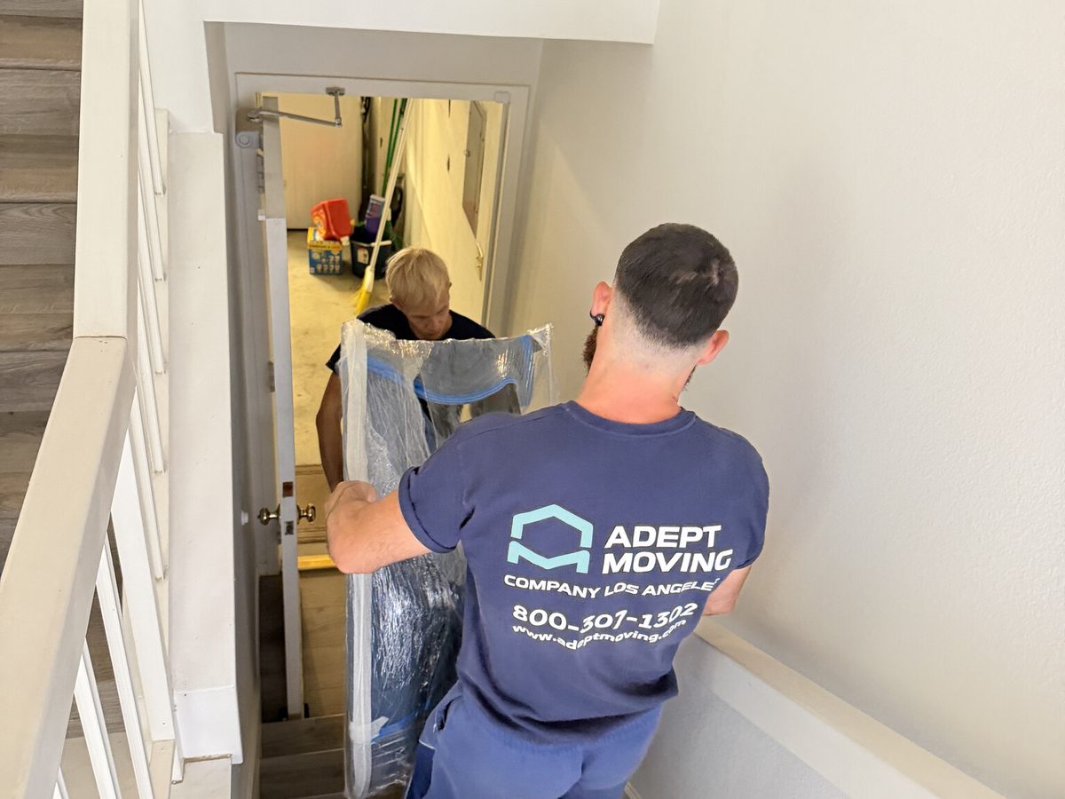 Adept Moving movers carrying a wrapped piece of furniture on the townhouse staircase