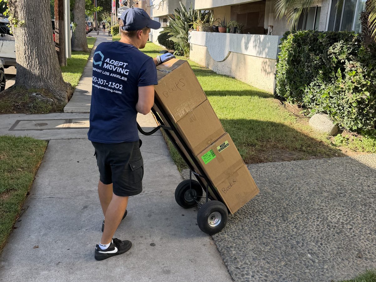 Adept Moving mover pushing boxes on a hand truck along the walkway on Hayvenhurst Avenue